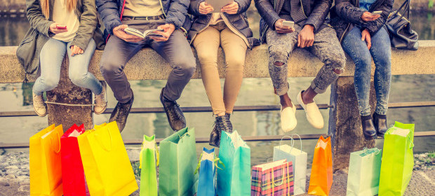 Group of 5 people sitting on a wall with many coloured shopping bags at their feet