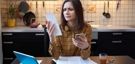 A woman in her kitchen examining a receipt in her hand