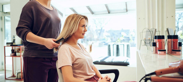 A woman sitting in a salon chair with a hairdresser holding her hair