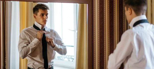 A young man tying his tie over his shirt in a mirror