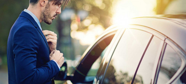 A man fixing his suit tie in a car window reflection