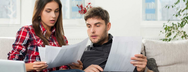 A young couple sitting on a couch concerned with credit reporting papers