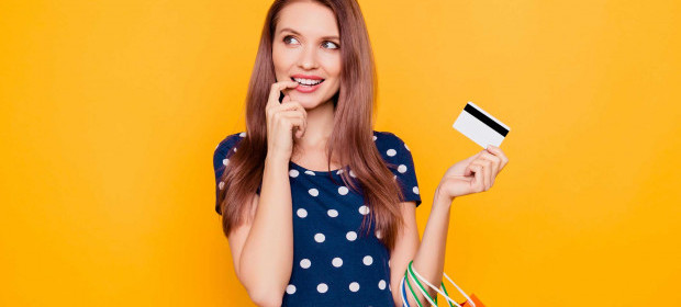 A woman with her credit card in her hand and her other finger at her mouth 