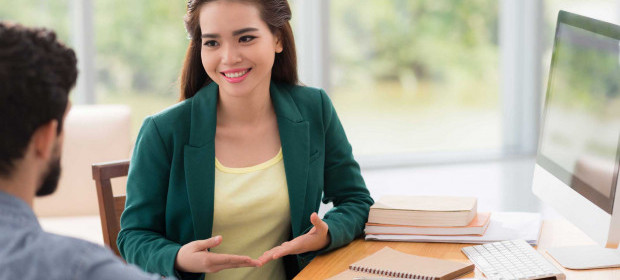 A woman sitting at a desk speaking to a man beside her