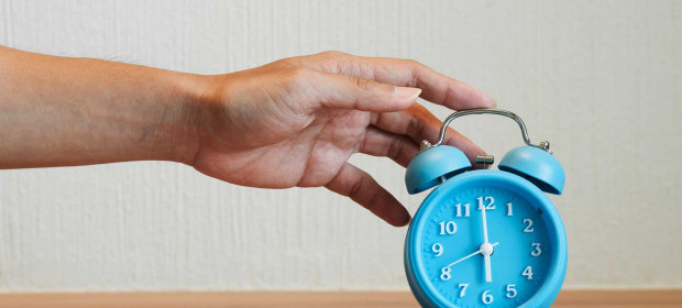 A hand reaching out to a blue alarm clock